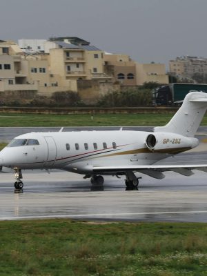 A private jet taxis on a wet runway at an airport with buildings in the background.